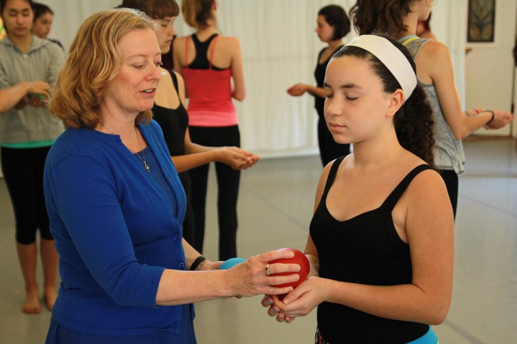 Susan holding out a red ball to a girl whose eyes are closed